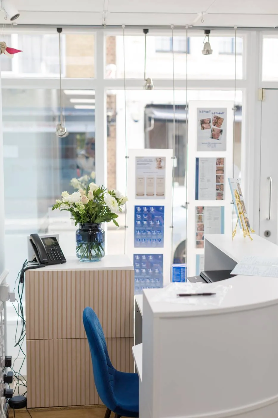 The reception desk at Cosmetic Medicine, with flowers and the Station Road window behind
