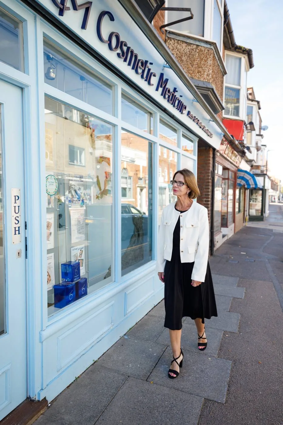 A woman in her 60s in a white jacket walks past the Cosmetic Medicine clinic on Station Road, Birchington