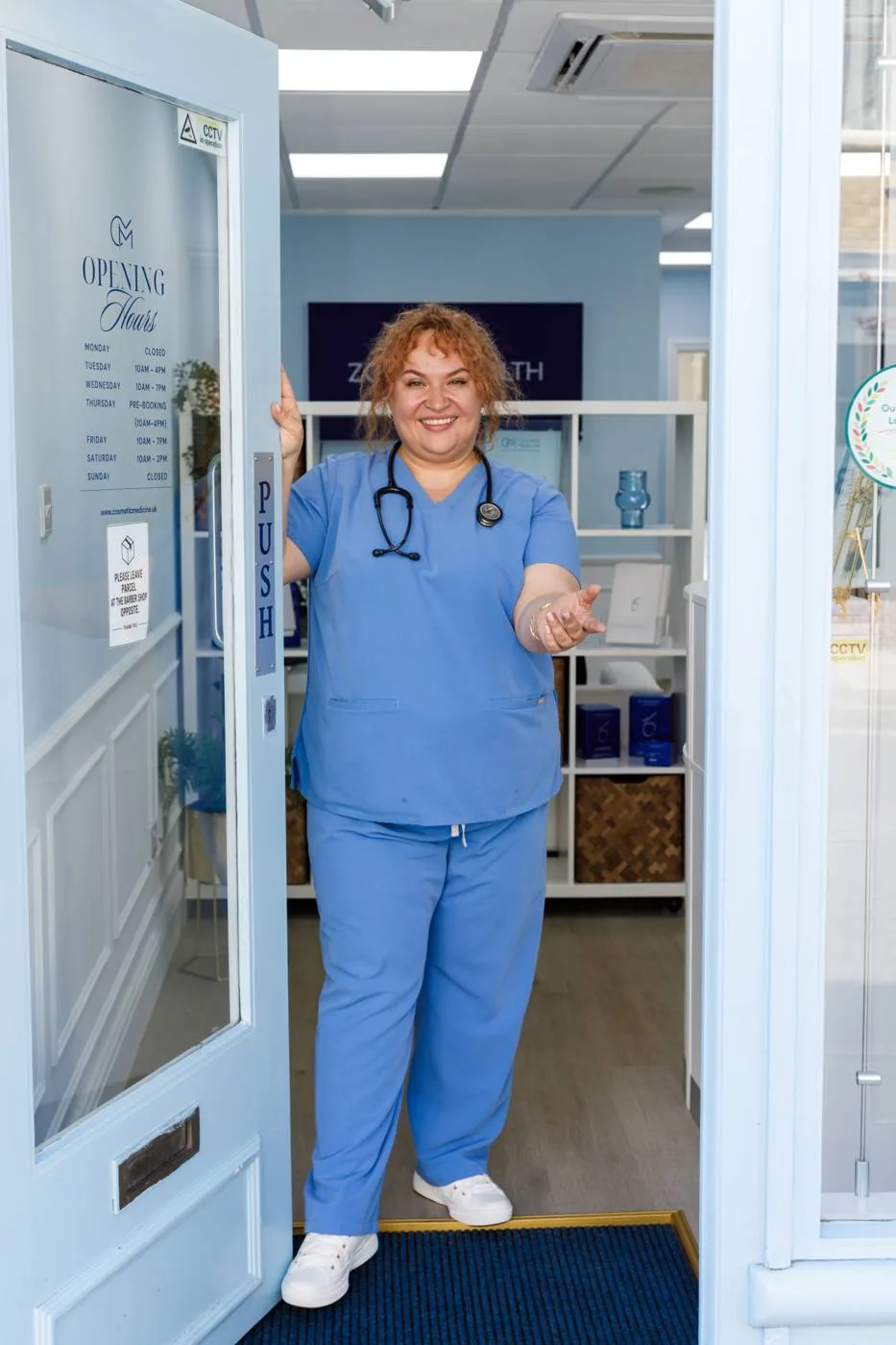 Dr Tania Robakowska in blue scrubs with a stethoscope, welcoming a patient at the clinic door