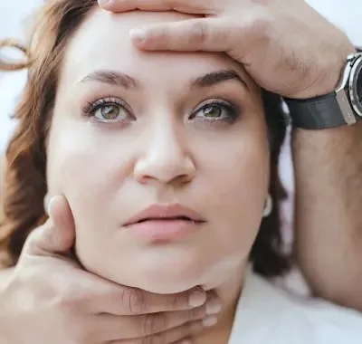A doctor's hands gently supporting a patient's forehead and jaw during a facial assessment